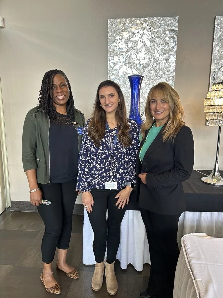 Three event attendees pose together in front of framed artwork.