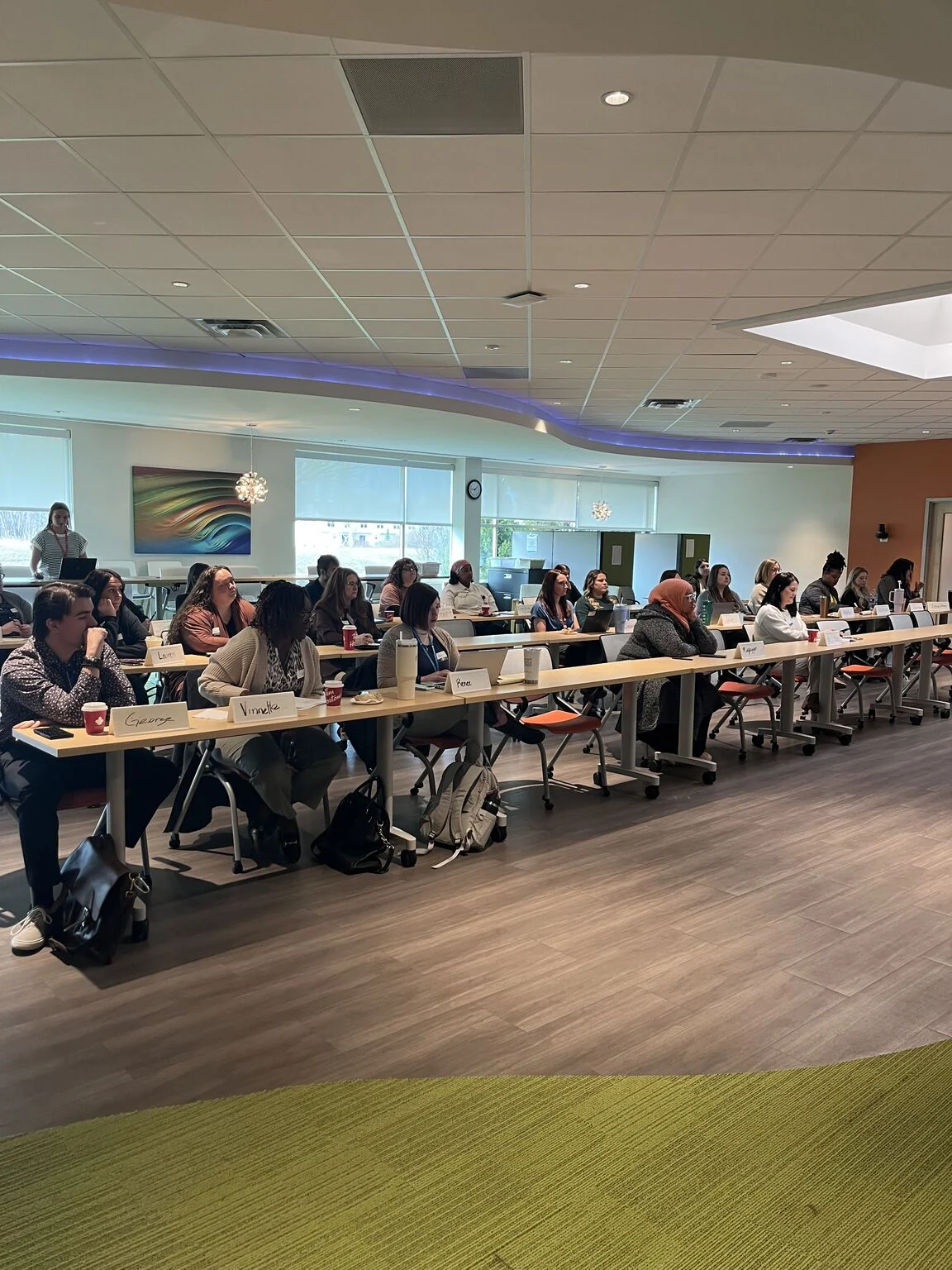 Communication training participants sit at long tables in a meeting room.
