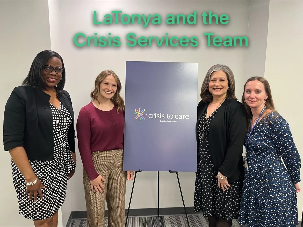 Four attendees pose beside a Crisis to Care display under a caption naming the Crisis Services team.