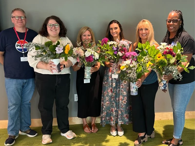Six team members hold flower arrangements made during a team activity.